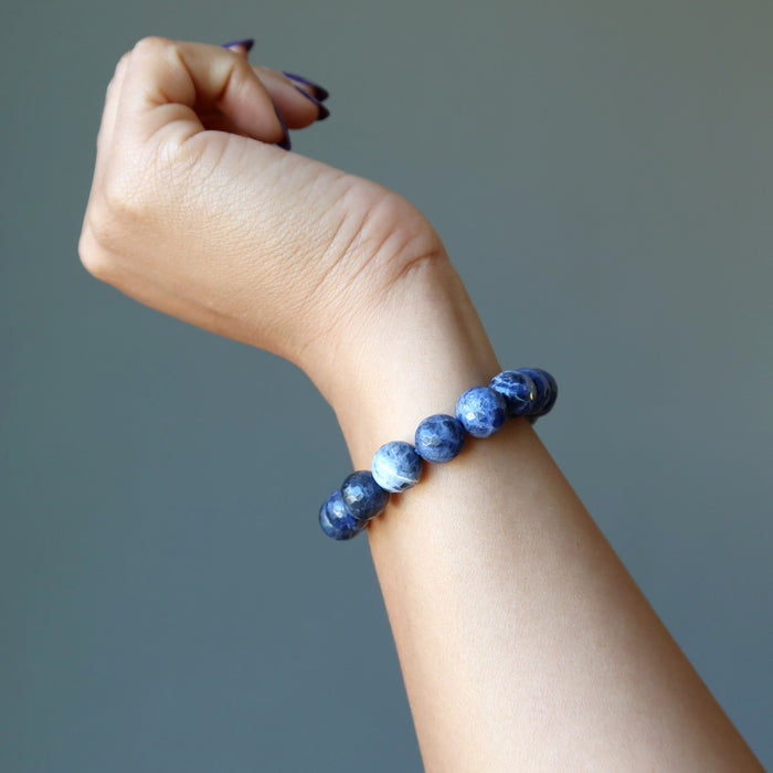 model raising hand wearing faceted round beaded sodalite bracelet on wrist