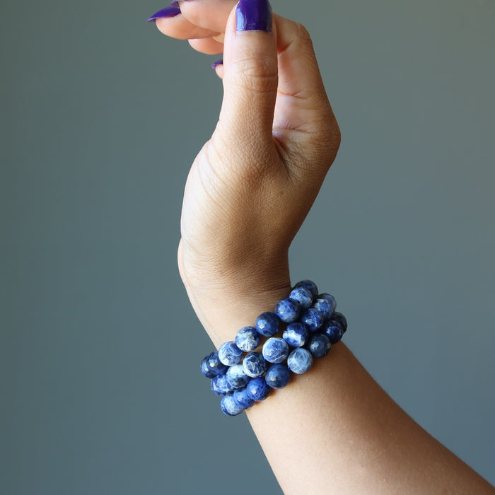 model raising hand wearing 3 faceted round beaded sodalite bracelets on wrist