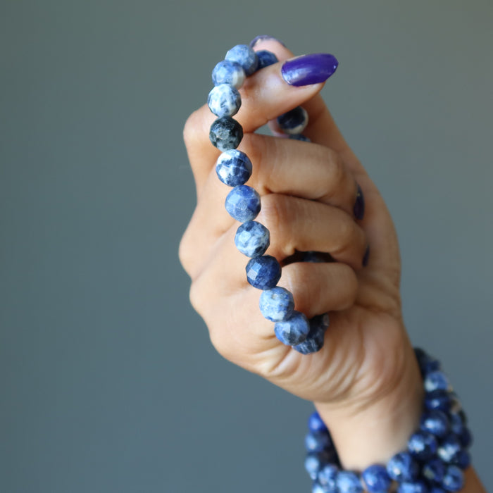 model holding one bracelet and  wearing 3 sodalite bracelets on wrist