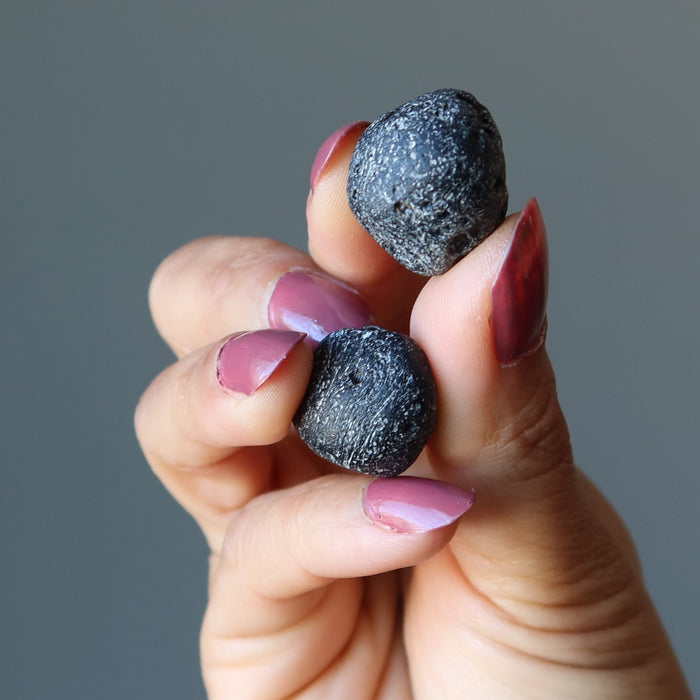 holding a pair of Two Round Black Tektite Meteorites 