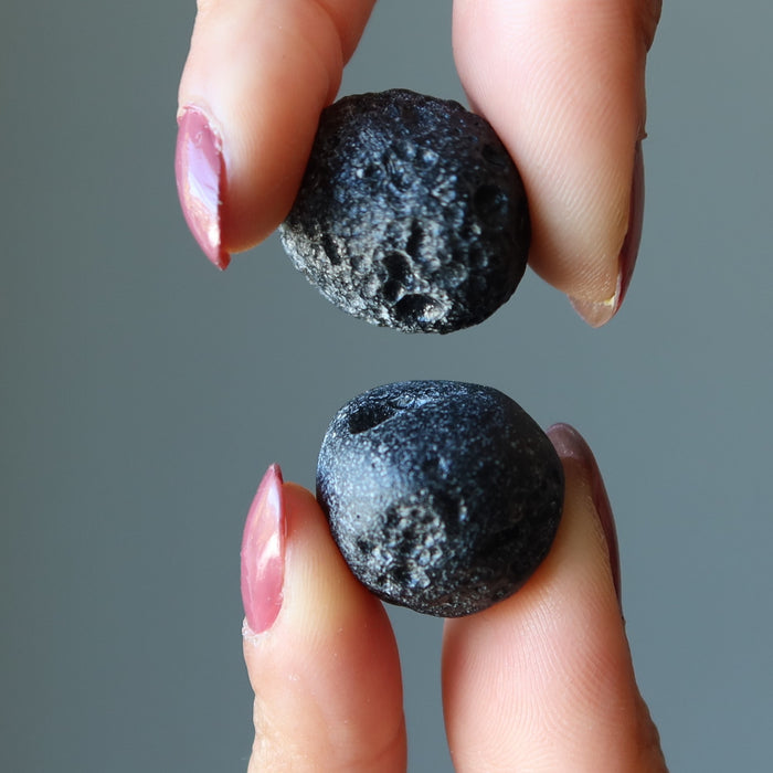 holding a pair of Two Round Black Tektite Meteorites 