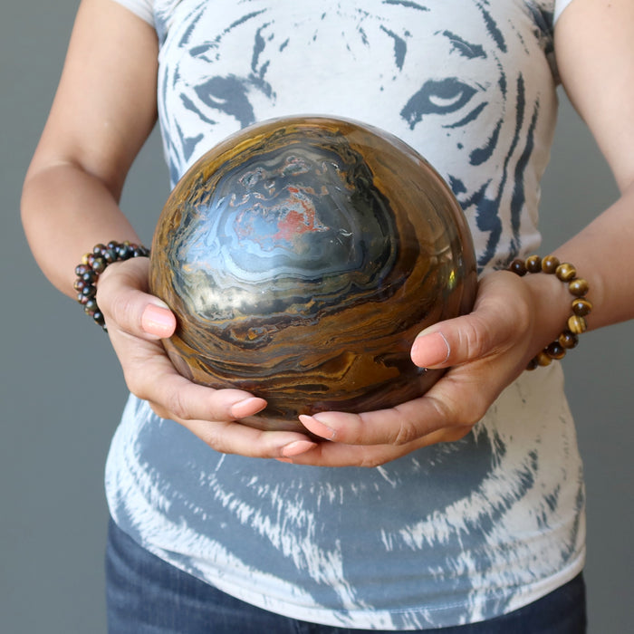 sheila of satin crystals holding a giant brown tiger iron sphere with veins of black hematite