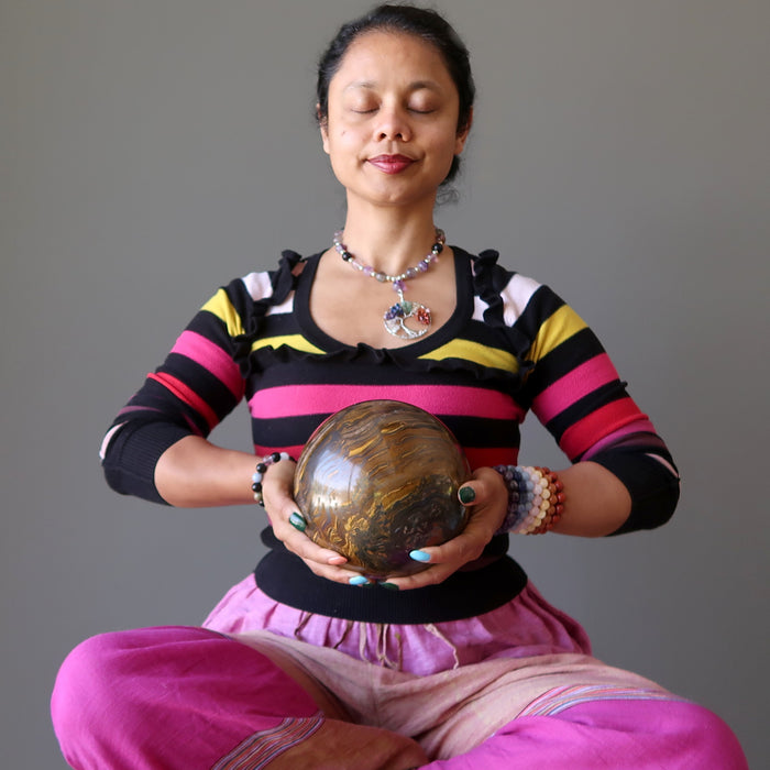 sheila of satin crystals meditating with a giant brown tigers eye sphere with veins of black hematite