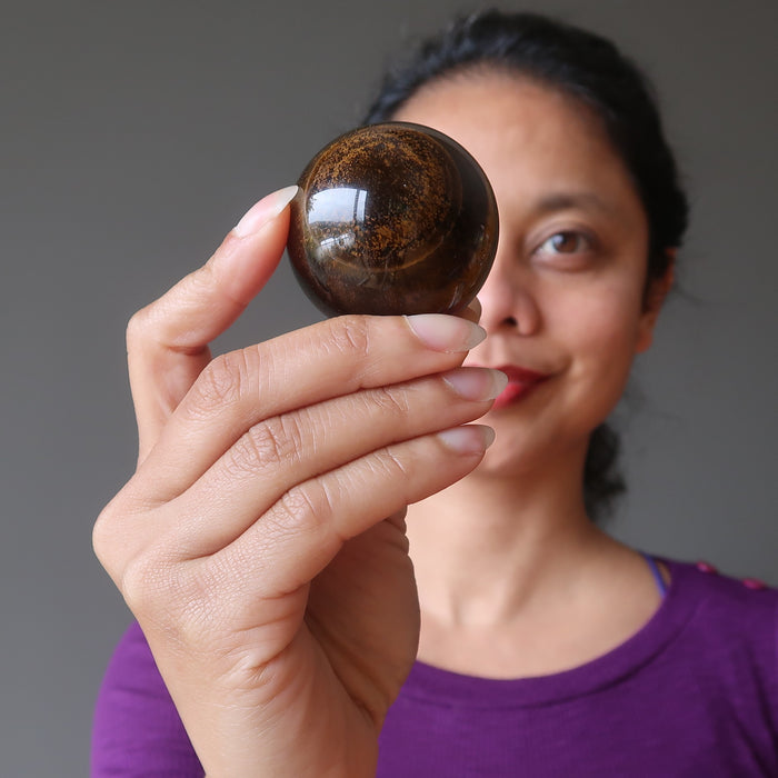 female model holding up golden tigers eye sphere