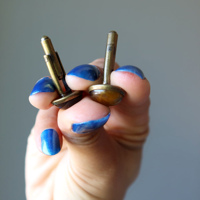 hand holding golden brown tigers eye in antique bronze cufflinks