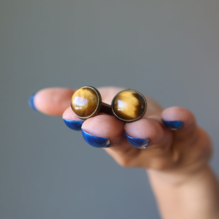 hand holding golden brown tigers eye in antique bronze cufflinks