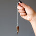 hand holding sterling silver tigers eye pendulum