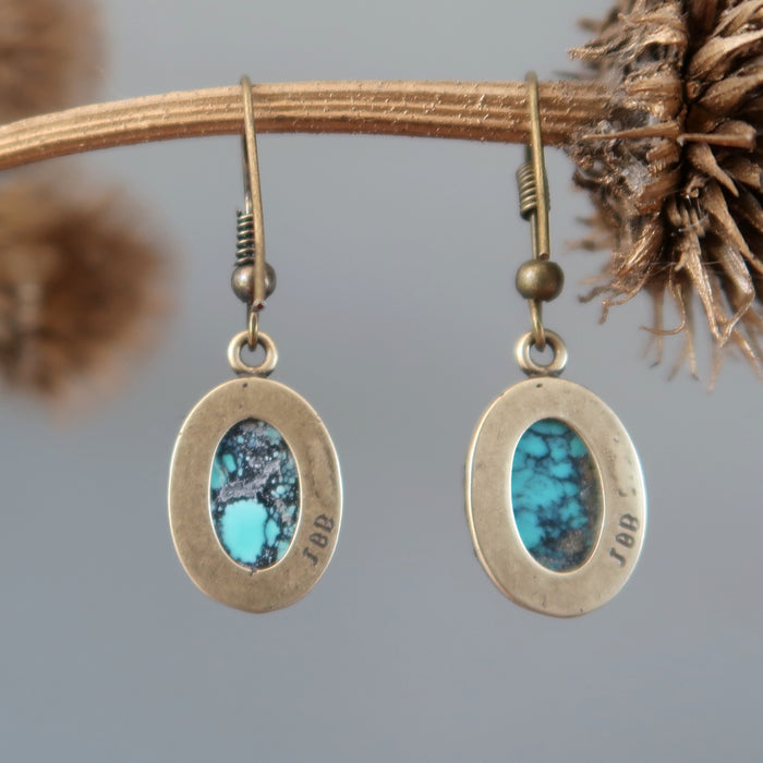 back of a pair of Blue Oval Antiqued Leaf Turquoise Earrings hanging on the dry brown branch