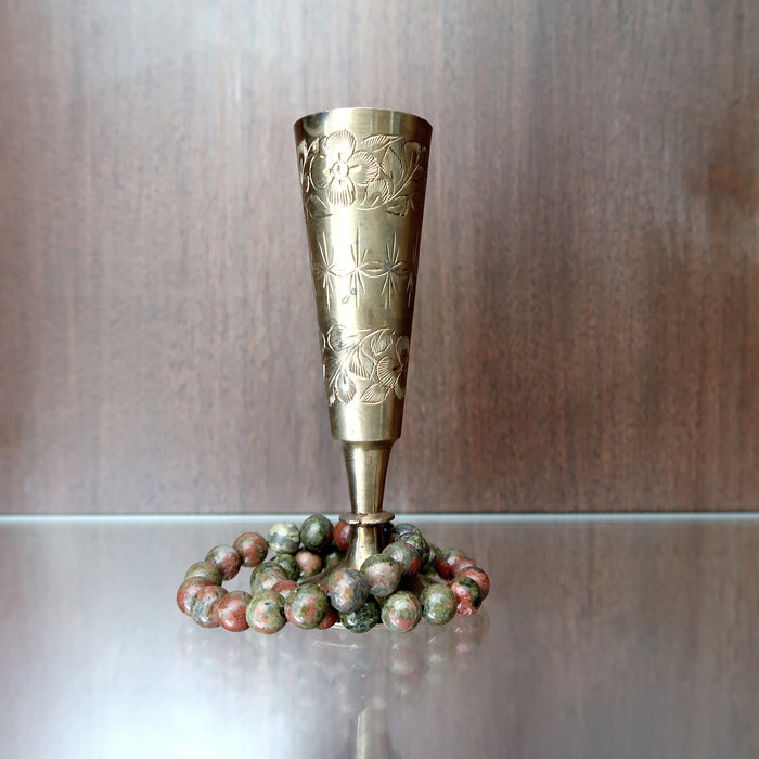 2 pink and green round unakite beaded stretch bracelets at the base of a metal chalice