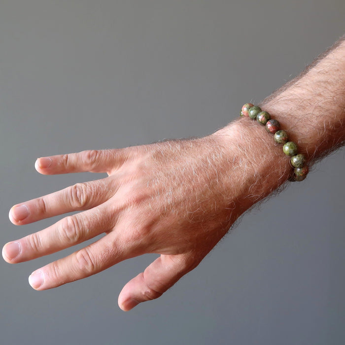 man's hand wearing pink and green round unakite beaded stretch bracelet